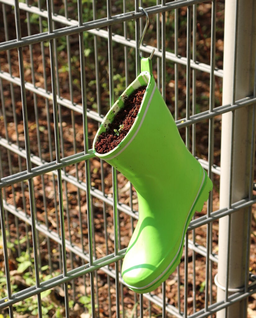 Das Foto zeigt einen grünen Gummistiefel am Zaun