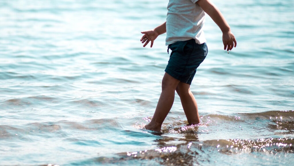Das Foto zeigt ein Kind, das mit den Füßen im Wasser steht