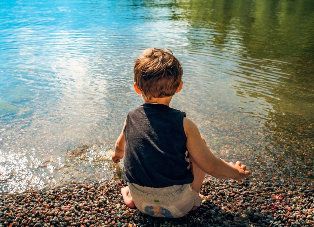Das Foto zeigt ein Kind, das am Wasser sitzt