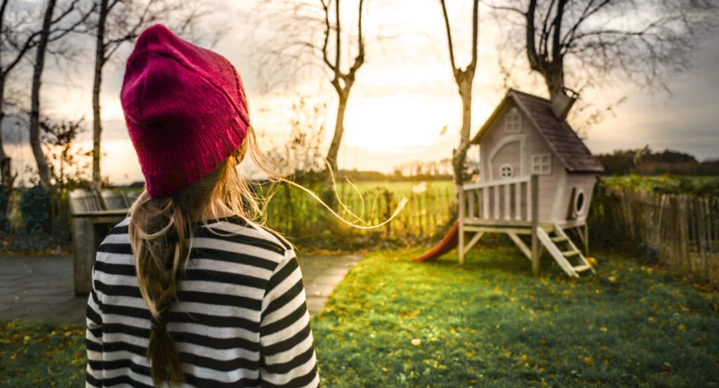 Das Foto zeigt ein Mädchen neben einem Baumhaus
