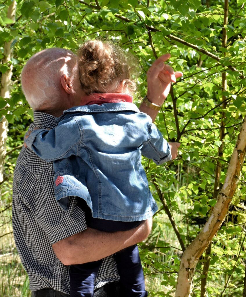 Das Foto zeigt einen Mann mit einem Kind auf dem Arm, sie schauen einen Baum an